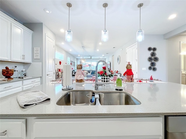 kitchen with hanging light fixtures, sink, white cabinets, and light stone counters