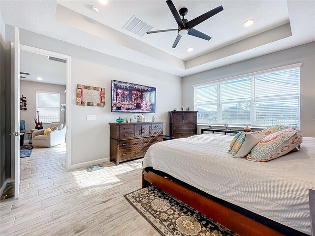 bedroom featuring ceiling fan, light wood-type flooring, and a tray ceiling