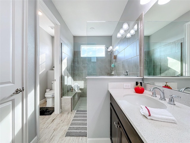 bathroom with a tile shower, vanity, hardwood / wood-style flooring, and toilet