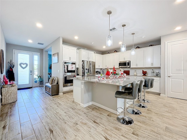 kitchen with decorative light fixtures, a kitchen breakfast bar, an island with sink, stainless steel appliances, and white cabinets