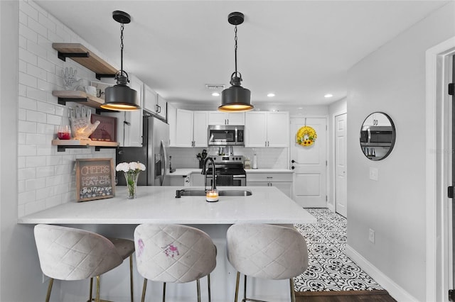 kitchen with appliances with stainless steel finishes, pendant lighting, white cabinetry, a breakfast bar area, and kitchen peninsula