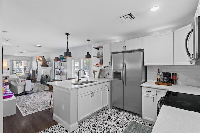 kitchen with sink, stainless steel appliances, white cabinets, a brick fireplace, and kitchen peninsula