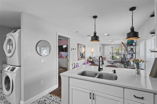 kitchen with white cabinetry, sink, hanging light fixtures, stacked washer / drying machine, and light stone countertops