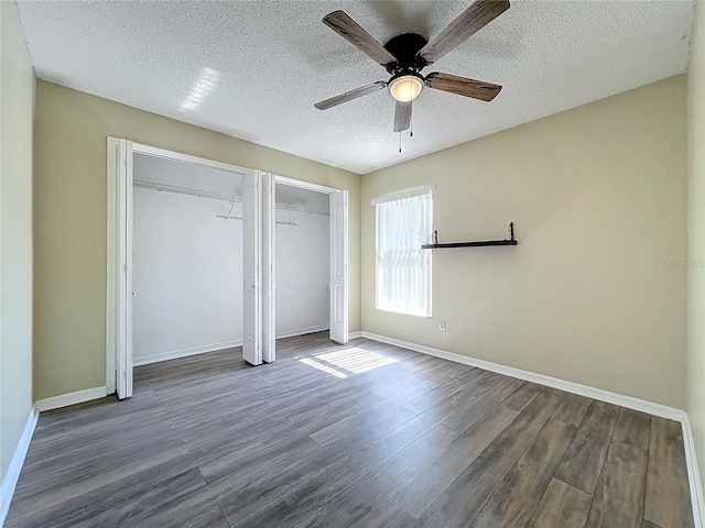 unfurnished bedroom featuring multiple closets, ceiling fan, dark hardwood / wood-style flooring, and a textured ceiling