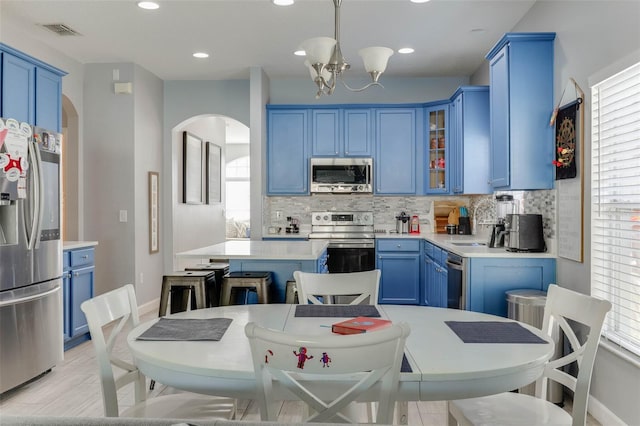 kitchen featuring blue cabinetry, tasteful backsplash, a chandelier, pendant lighting, and stainless steel appliances