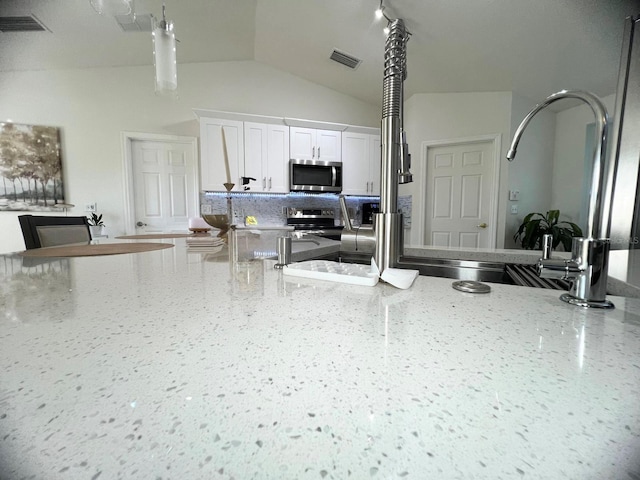 kitchen with stainless steel appliances, lofted ceiling, white cabinets, and light stone counters