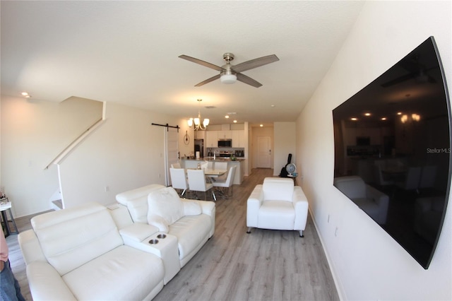 living room featuring ceiling fan with notable chandelier, a barn door, and light hardwood / wood-style floors