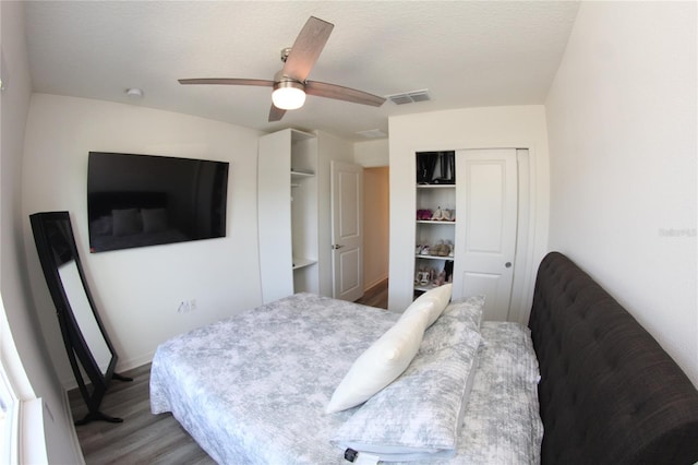 bedroom with ceiling fan, two closets, a textured ceiling, and light wood-type flooring