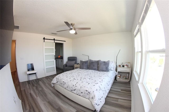 bedroom featuring ceiling fan, dark hardwood / wood-style floors, a barn door, and a textured ceiling