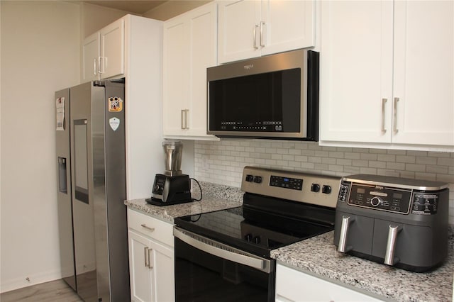 kitchen featuring light stone countertops, white cabinetry, appliances with stainless steel finishes, and backsplash