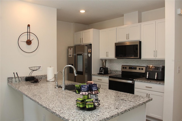 kitchen featuring appliances with stainless steel finishes, light stone countertops, kitchen peninsula, and white cabinets