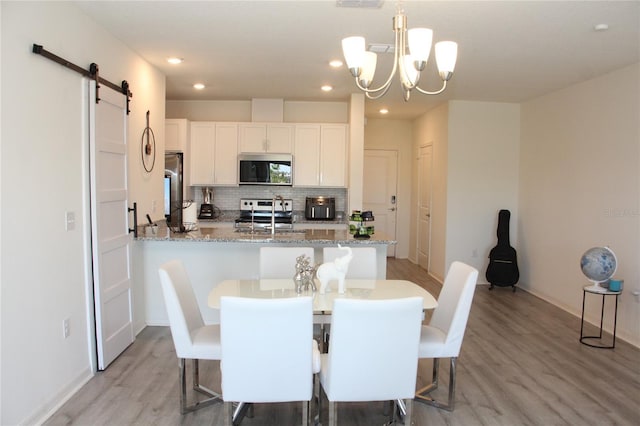 dining space featuring an inviting chandelier, a barn door, sink, and light hardwood / wood-style flooring