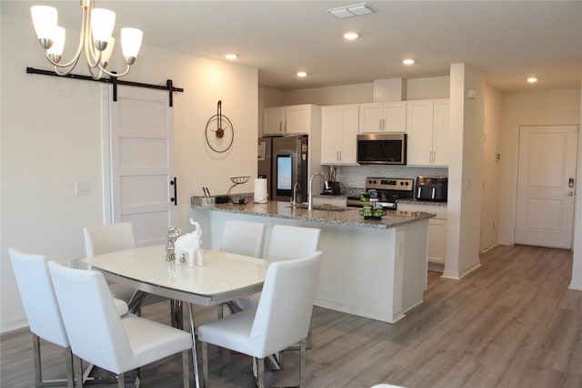 kitchen with sink, dark stone counters, stainless steel appliances, a barn door, and white cabinets