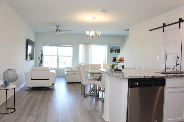 kitchen with pendant lighting, sink, white cabinetry, stainless steel dishwasher, and a barn door