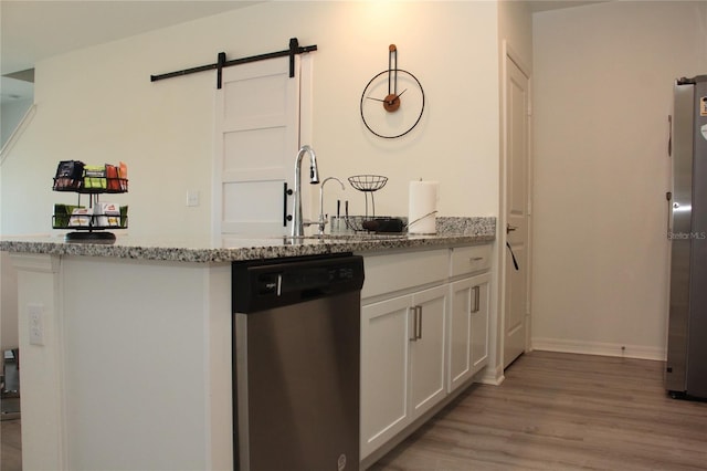 kitchen with appliances with stainless steel finishes, light stone countertops, white cabinets, a barn door, and light wood-type flooring