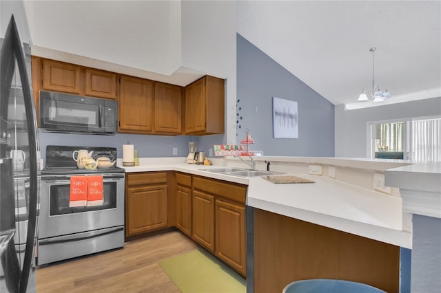 kitchen with vaulted ceiling, pendant lighting, sink, black appliances, and light hardwood / wood-style flooring