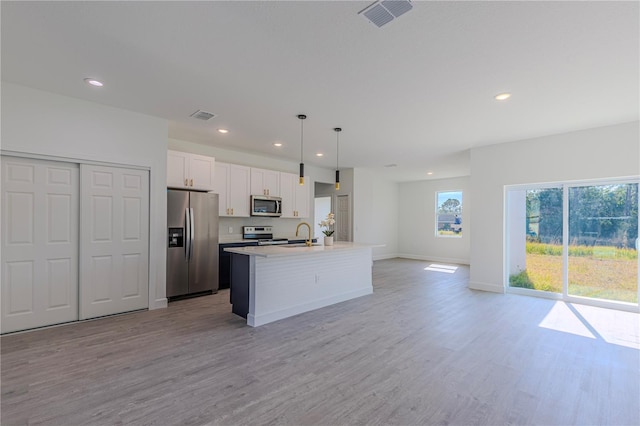 kitchen with decorative light fixtures, a center island with sink, appliances with stainless steel finishes, light hardwood / wood-style floors, and white cabinets