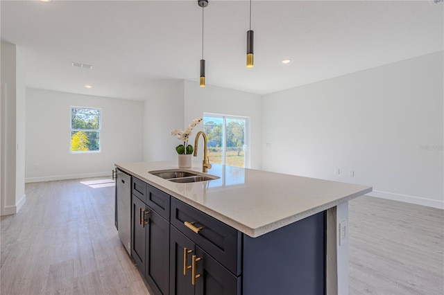 kitchen featuring a kitchen island with sink, sink, light wood-type flooring, and decorative light fixtures