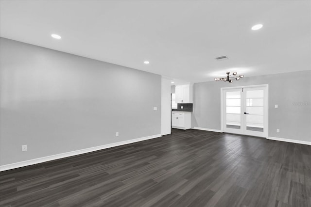 unfurnished living room featuring an inviting chandelier and dark hardwood / wood-style flooring