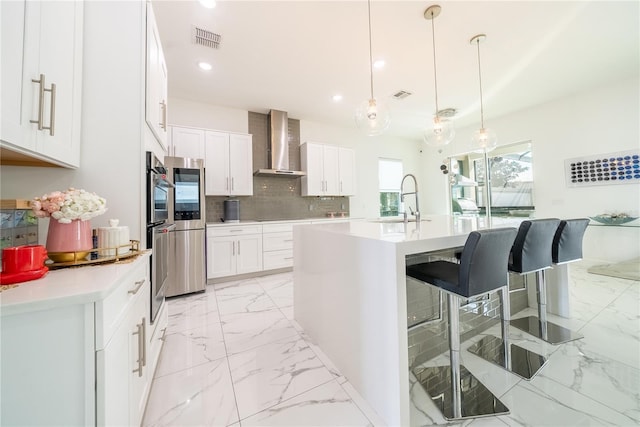 kitchen featuring sink, white cabinets, decorative backsplash, hanging light fixtures, and wall chimney range hood