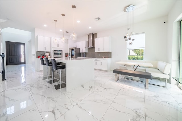 kitchen with wall chimney range hood, hanging light fixtures, white cabinets, and a center island