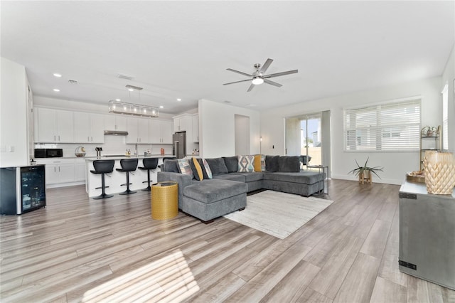 living room with wine cooler, ceiling fan, and light hardwood / wood-style flooring