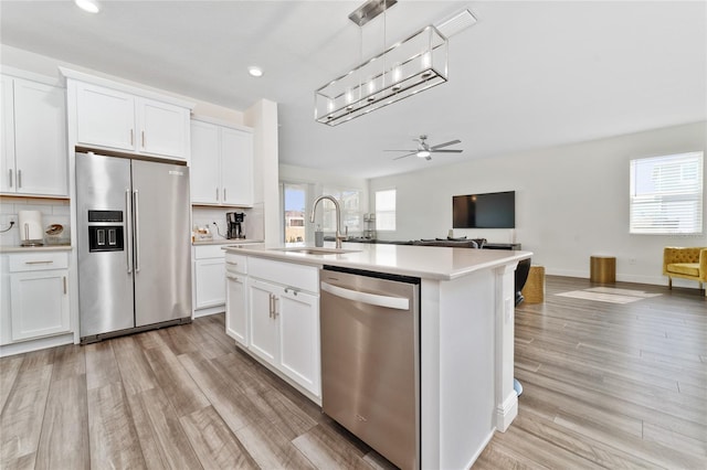 kitchen featuring sink, appliances with stainless steel finishes, hanging light fixtures, white cabinets, and a center island with sink