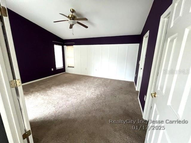 unfurnished bedroom featuring ceiling fan, vaulted ceiling, and dark colored carpet