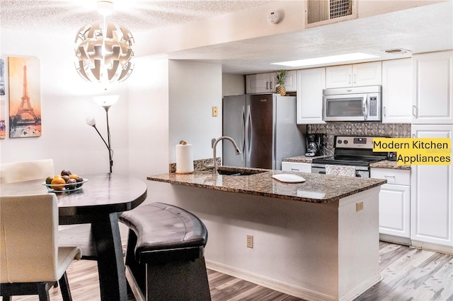 kitchen featuring sink, decorative light fixtures, dark stone counters, stainless steel appliances, and white cabinets