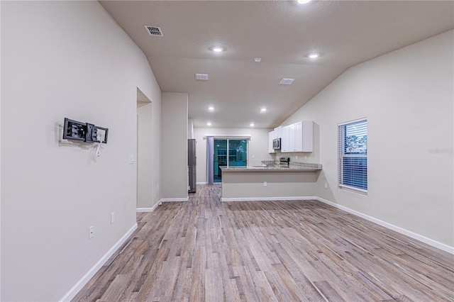 unfurnished living room with lofted ceiling, a textured ceiling, and light wood-type flooring