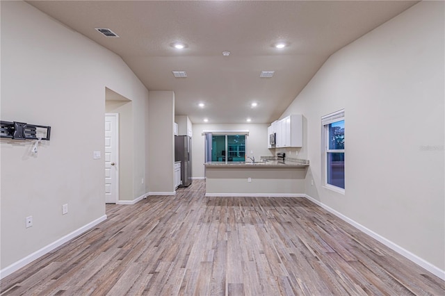 unfurnished living room with sink, vaulted ceiling, a textured ceiling, and light wood-type flooring