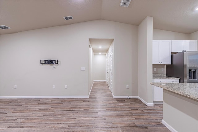 kitchen with stainless steel refrigerator with ice dispenser, light stone counters, white cabinets, vaulted ceiling, and light wood-type flooring