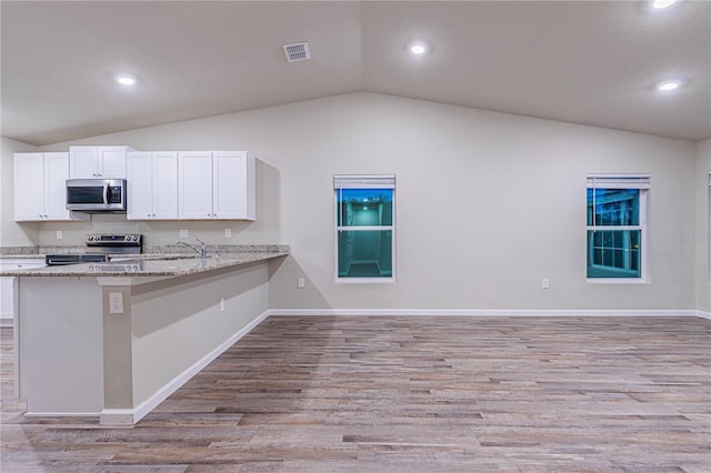 kitchen with stainless steel appliances, light stone countertops, lofted ceiling, and kitchen peninsula