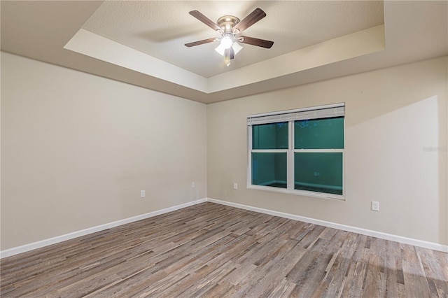 unfurnished room featuring hardwood / wood-style floors, a tray ceiling, a textured ceiling, and ceiling fan