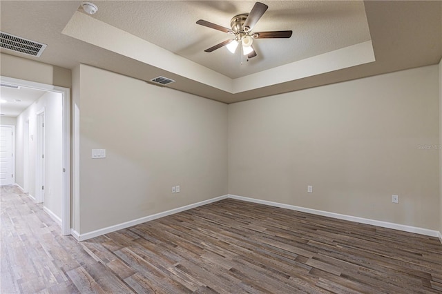 empty room featuring a raised ceiling, ceiling fan, hardwood / wood-style floors, and a textured ceiling