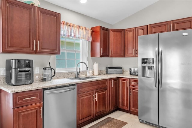 kitchen with sink, light tile patterned floors, appliances with stainless steel finishes, light stone countertops, and vaulted ceiling