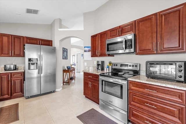 kitchen with light tile patterned floors, vaulted ceiling, light stone countertops, and appliances with stainless steel finishes