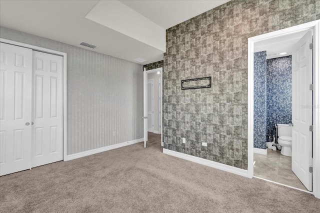 unfurnished bedroom with a closet, ensuite bathroom, and light carpet