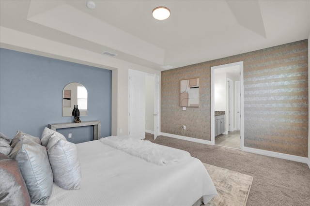 bedroom featuring a tray ceiling, ensuite bath, and light colored carpet