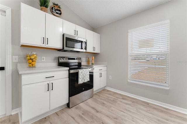 kitchen featuring vaulted ceiling, a textured ceiling, light wood-type flooring, appliances with stainless steel finishes, and white cabinets