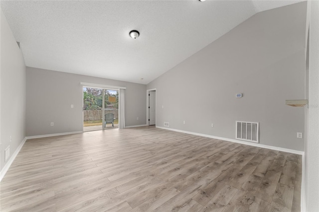 unfurnished room with vaulted ceiling, a textured ceiling, and light wood-type flooring