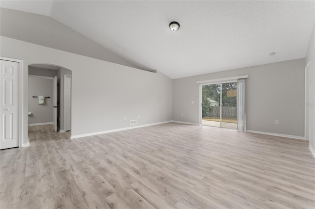 unfurnished room with vaulted ceiling, a textured ceiling, and light hardwood / wood-style floors