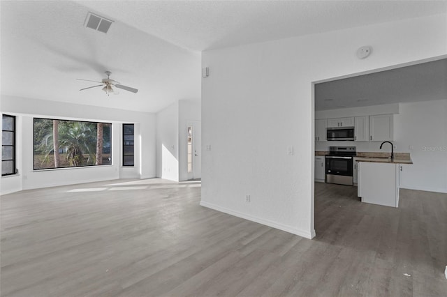 unfurnished living room featuring ceiling fan, light hardwood / wood-style floors, sink, and a textured ceiling