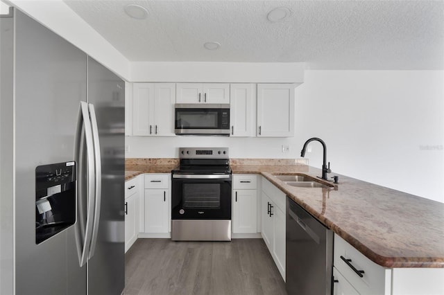 kitchen featuring appliances with stainless steel finishes, white cabinetry, sink, kitchen peninsula, and light wood-type flooring