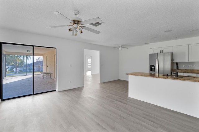 unfurnished living room with ceiling fan, sink, light hardwood / wood-style flooring, and a textured ceiling