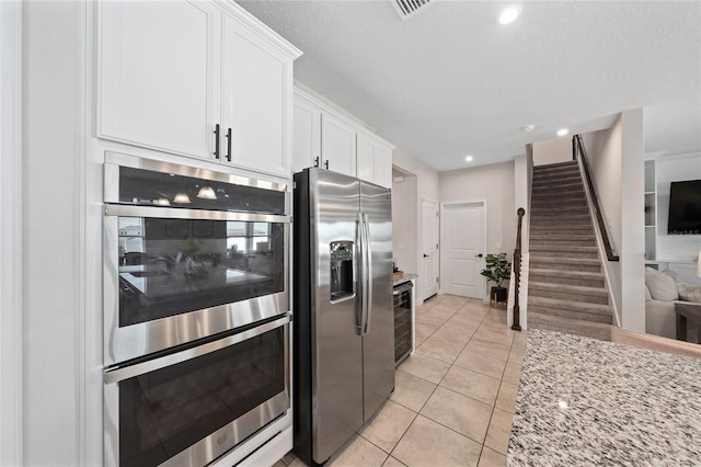 kitchen with light stone counters, light tile patterned floors, stainless steel appliances, beverage cooler, and white cabinets