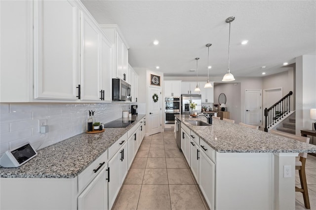 kitchen featuring white cabinetry, a large island with sink, hanging light fixtures, stainless steel appliances, and light stone countertops