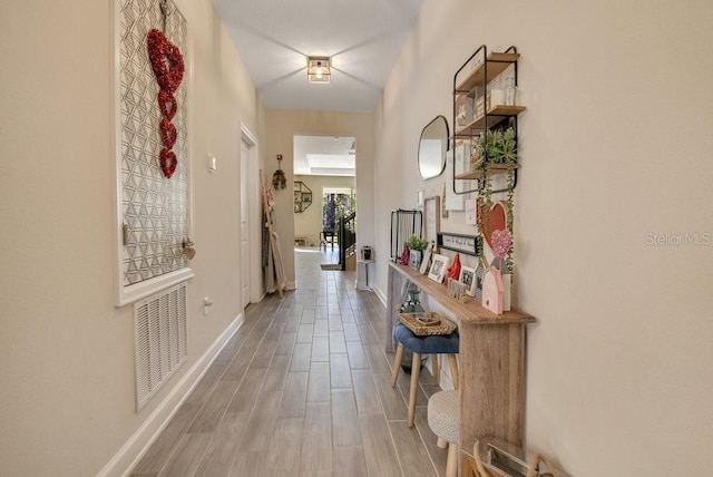 hall featuring wood finished floors, visible vents, and baseboards