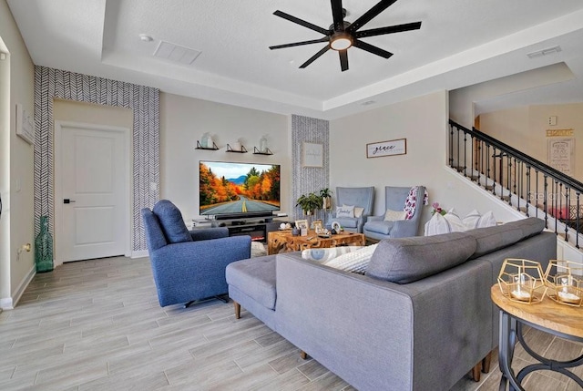 living room featuring stairs, ceiling fan, a tray ceiling, and wood tiled floor