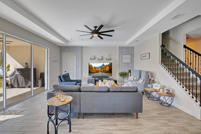 living area featuring ceiling fan, visible vents, stairs, wood tiled floor, and a raised ceiling